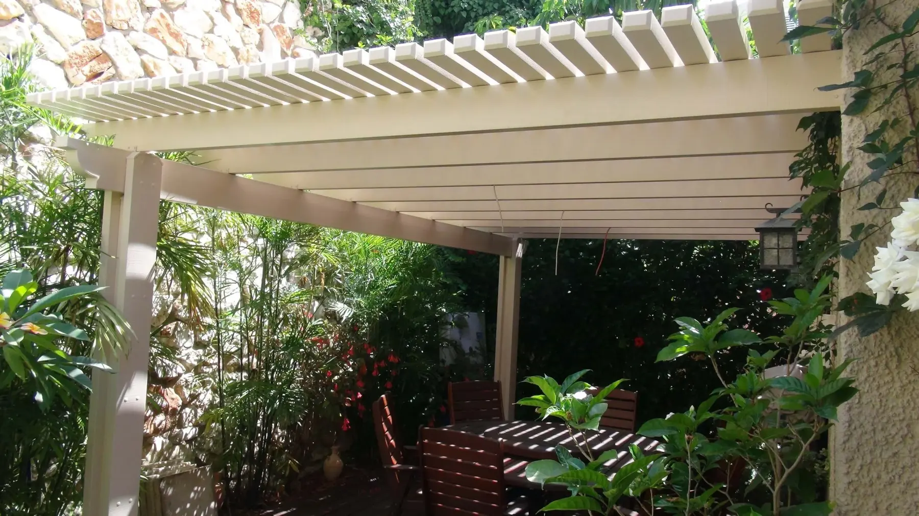 Light-colored Elite pergola sheltering a dining area in a lush garden